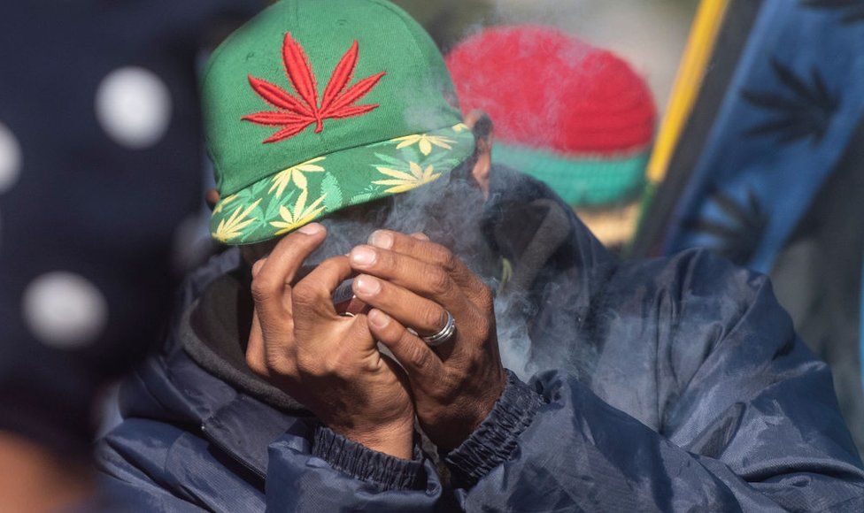 A man with a cannabis leaf motif on his hat smokes cannabis.
