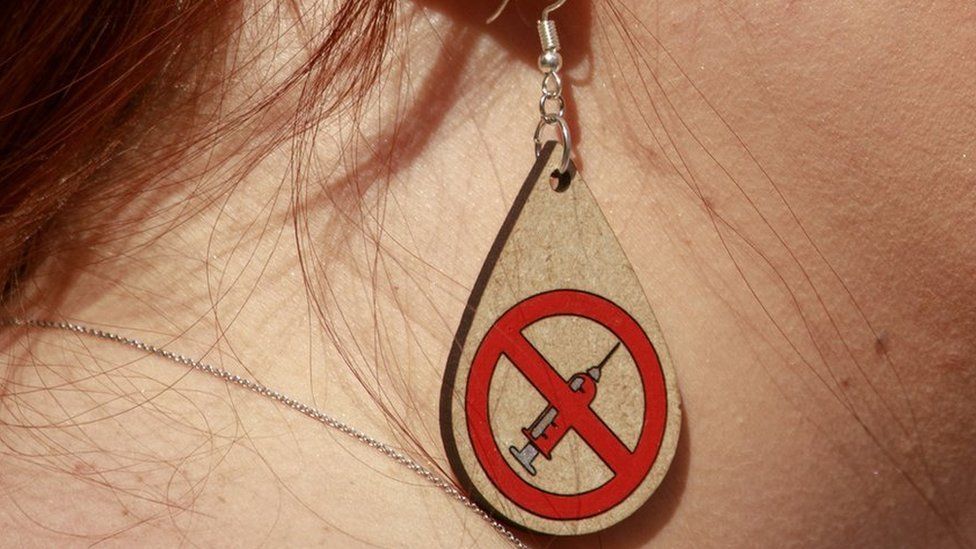 Anti-vax earring with a logo of a vaccine crossed out.