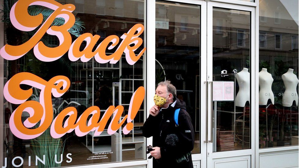 A man walks past a sign reading "Back Soon" in the window of a closed shop in Edinburgh city centre