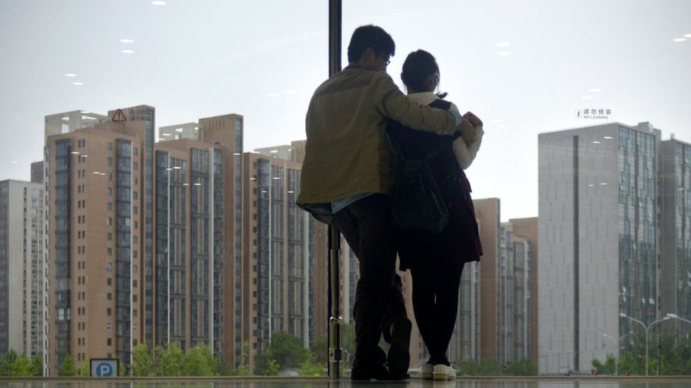 A couple look out of a window at blocks of flats in Beijing