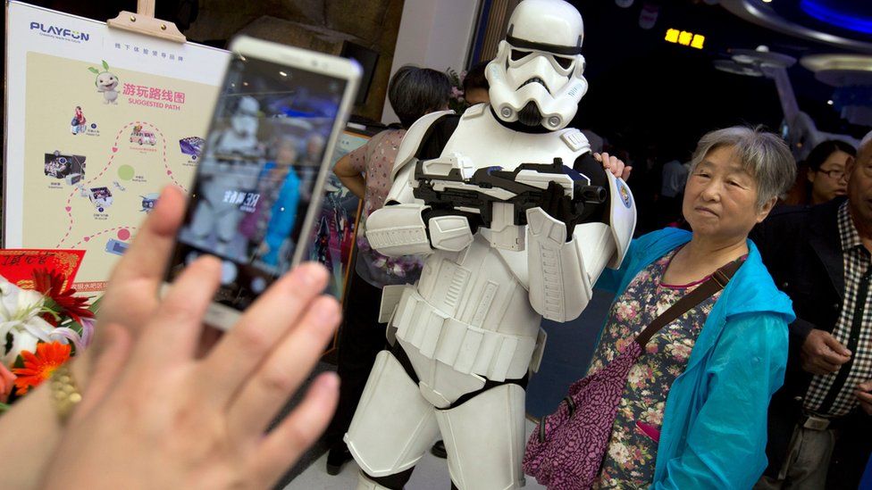 A Chinese woman poses for a smartphone photo with a worker dressed in a storm trooper costume at the Wanda Mall at the Wanda Cultural Tourism City in Nanchang in southeastern China"s Jiangxi province, Saturday, May 28, 2016.