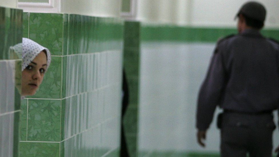 Иранский заключенный выглядывает из-за стены, когда охранник проходит мимо женского отделения печально известной тюрьмы Эвин