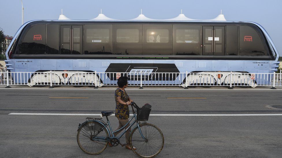 A woman pushes a bicycle looks at the Transit Elevated Bus TEB-1 conduct a test run after it unveiled in Qinhuangdao, north China's Hebei Province