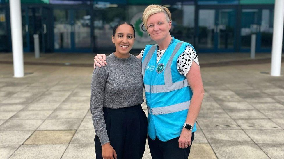 Hina Shafi and teacher Nicola Ponsonby stood outside Challney High School for Girls. Hina is on the left and is smiling, with her dark hair worn behind her ears. She is wearing a grey long-sleeved top with a dark navy trousers on. Nicola is stood next to her with her right arm around Hina's shoulder. She is smiling and has her short blonde hair worn over to one side. She is wearing a white top with black spots on it and a bright blue high-viz jacket over the top.