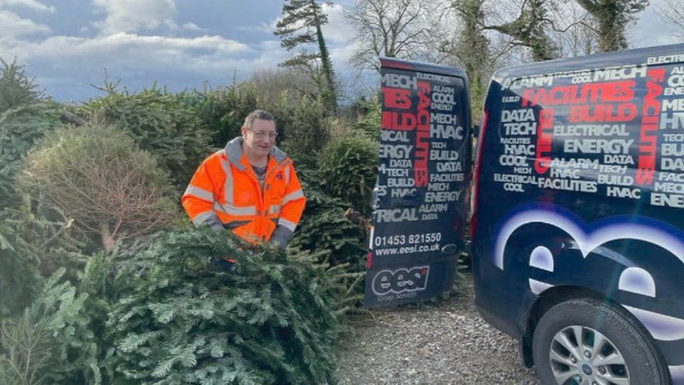 A man standing next to a van and some Christmas trees