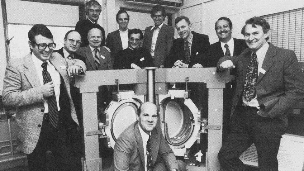Group of scientists stand around a model of the JET reactor in 1977