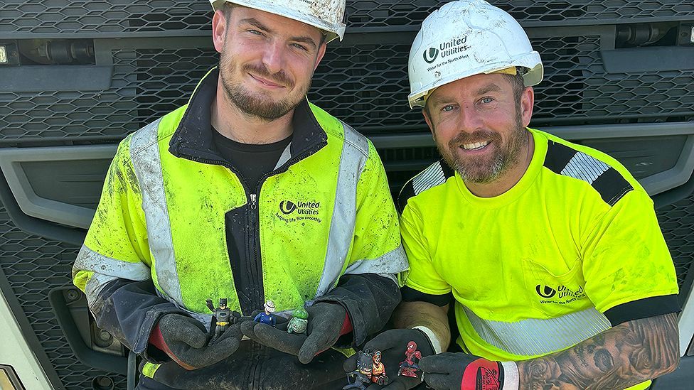 Andrew Bromley and David Cavill from United Utilities in front of a lorry wearing high-vis tops and helmets, holding some of the toys they have found in the sewers