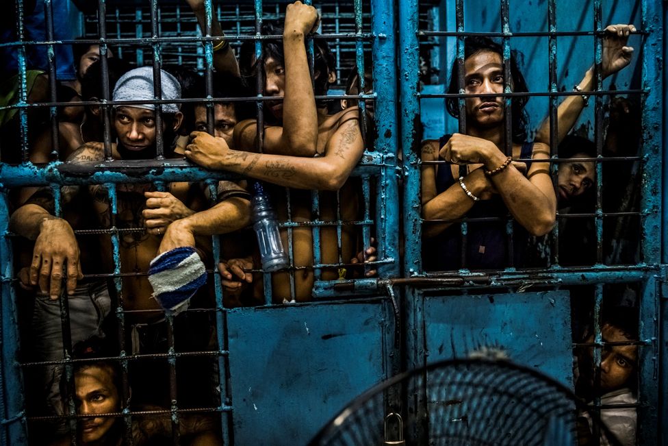 Inmates watch as drug suspects are processed inside a police station in Manila, Philippines
