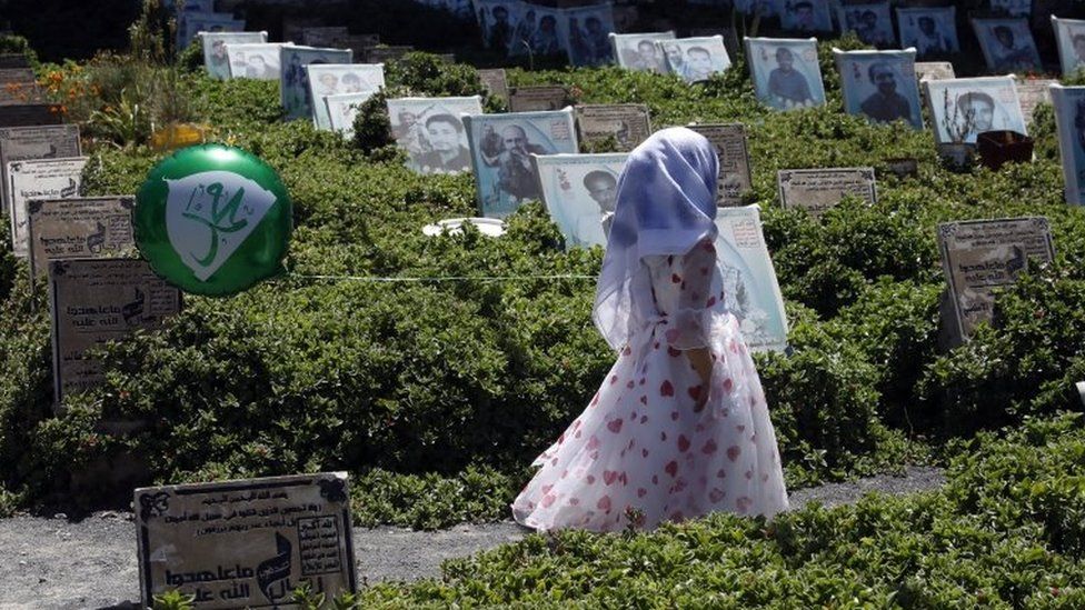 A Yemeni girl holding a balloon walks amongst the graves of slain Houthi fighters at a cemetery in Sanaa (15 October 2021)