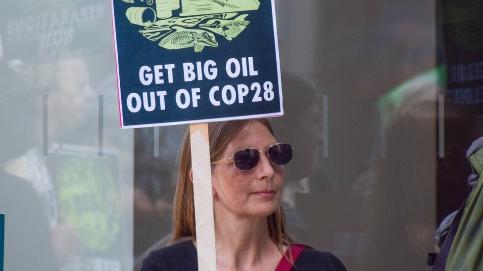 A climate activist holds a placard opposed to oil companies taking over COP28