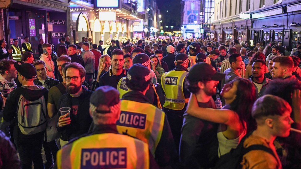 Police officers are seen walking through heavy crowds in Soho, central London