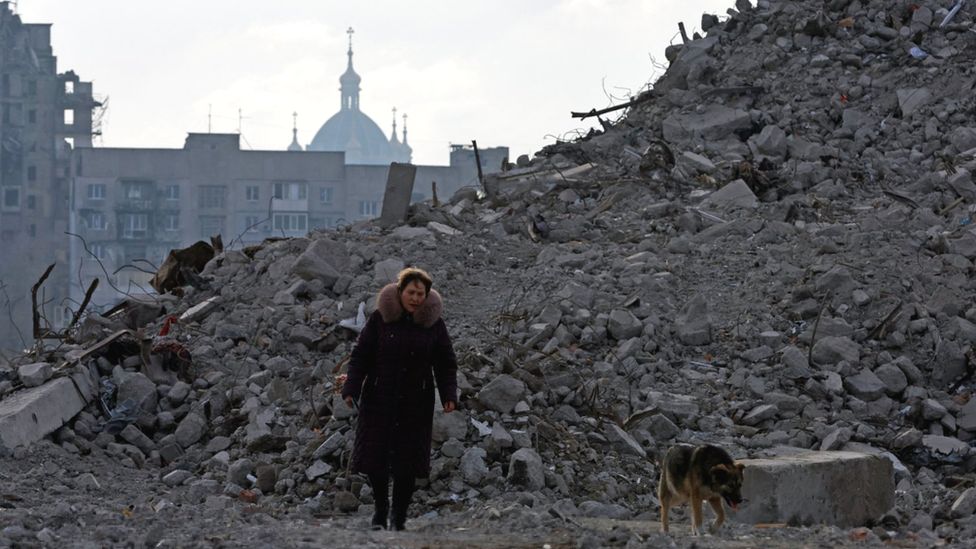 Женщина и собака гуляют по развалинам Мариуполя