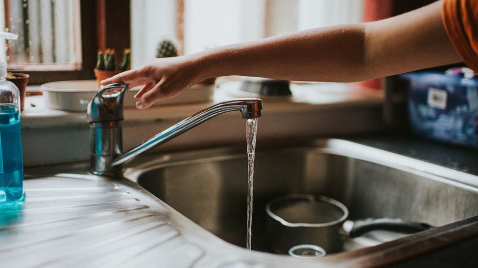 Hand turning off a Running Chrome Tap in a kitchen - stock photo