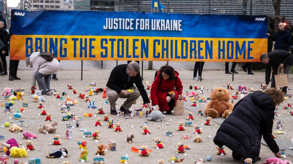 People light candles beside teddy bear in Schuman Roundabout, Brussels, on February 24, 2023
