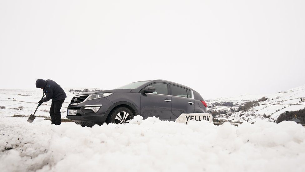 A man digs out a car in heavy snow in the Yorkshire Dales