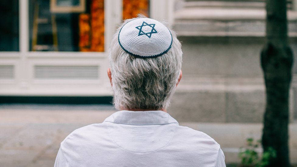 A Jewish man wearing a kippah sits on a bench in London