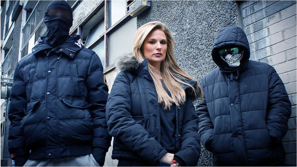 Livvy Haydock standing in the middle of two masked people involved in kidnap gangs