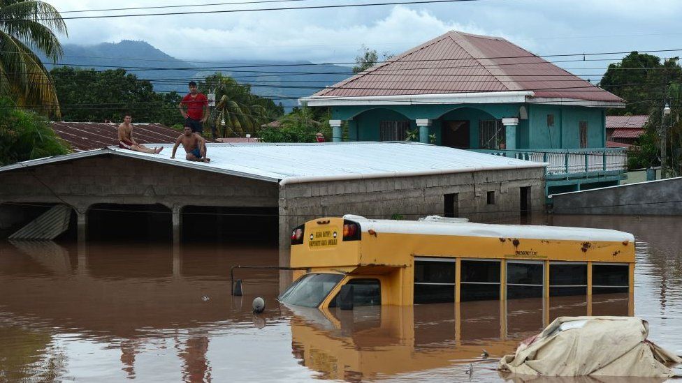 Men remain on a rooftop near a bus at a flooded street in Omonita, El Progreso