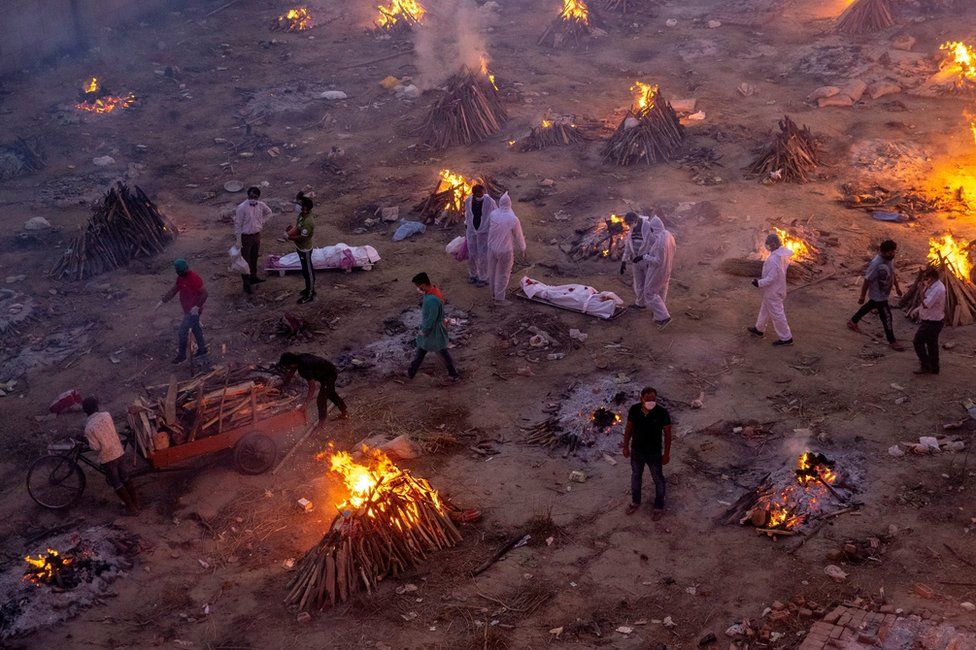 People wait to cremate Covid victims whilst surrounded by burning funeral pyres in New Delhi, India
