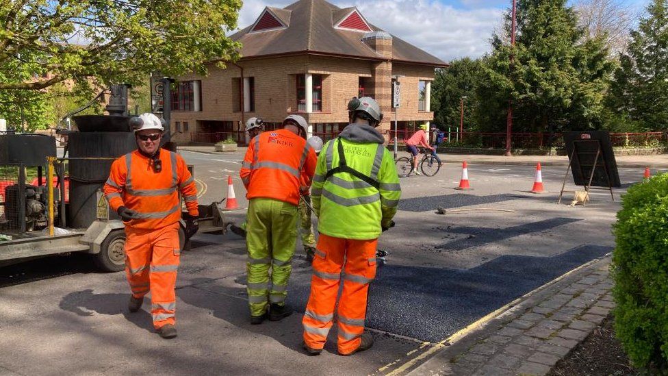 Men in orange and yellow hi-vis carrying out road repairs