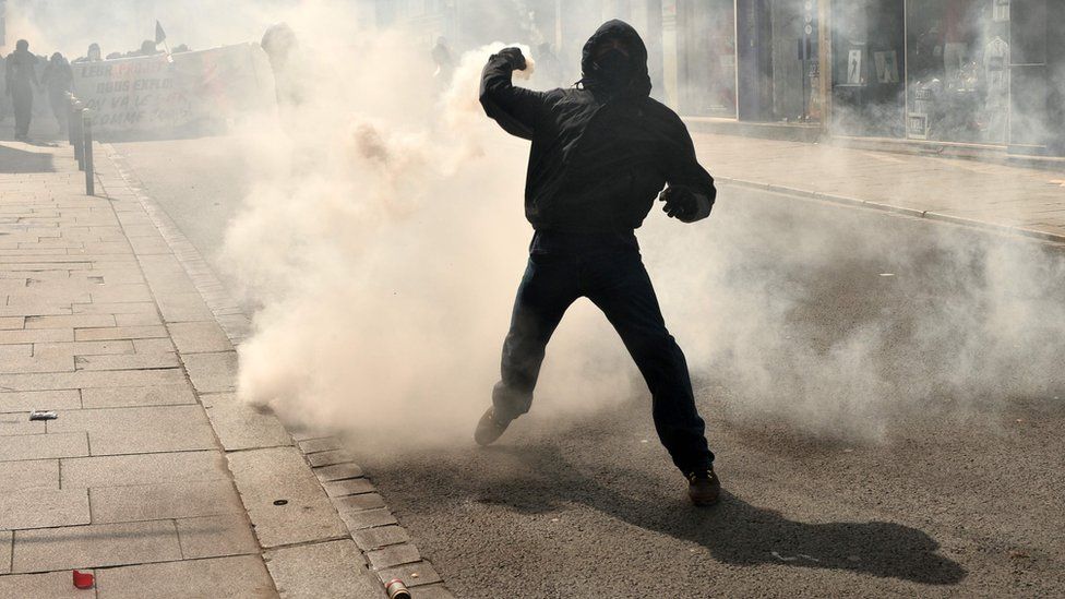 A protester lobs a tear gas canister back at riot police