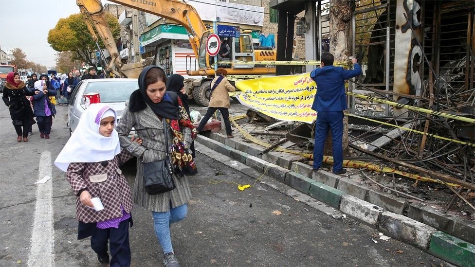 Women and girls walk past a burned out bank in Tehran, Iran (20 November 2019