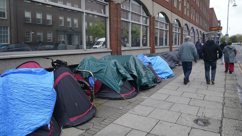 People walking past tents housing asylum seekers near to the International Protection Office, in Dublin