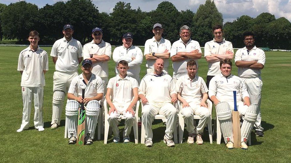 A team of cricketers in whites, lined up facing the camera