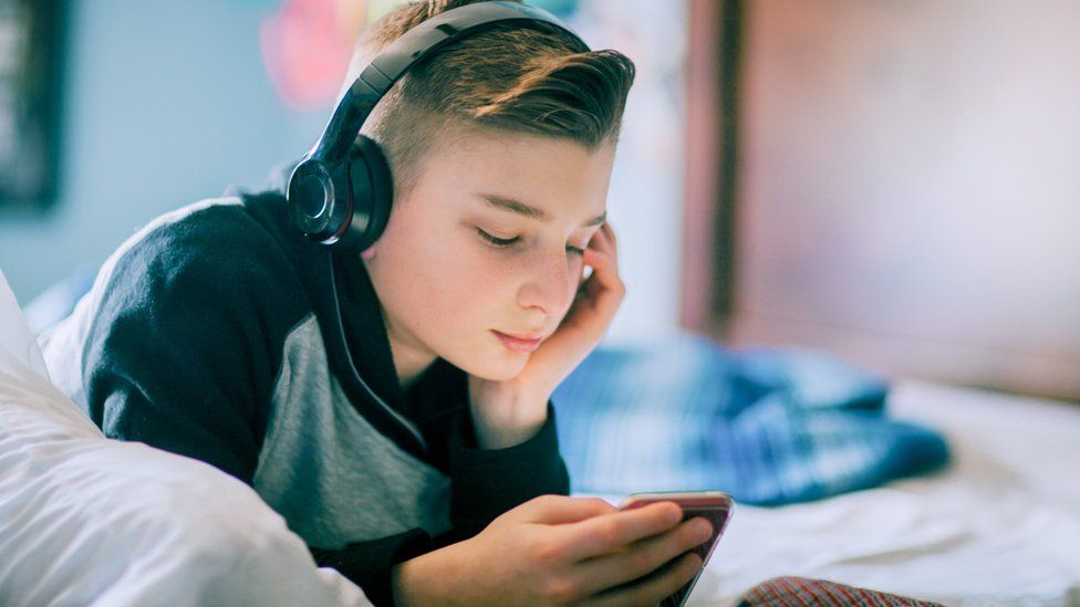 Teenage boy watching his phone, wearing headphones
