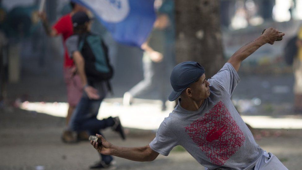 An anti-austerity protester throws a stone at police, outside the state legislature where lawmakers are discussing austerity measures in Rio de Janeiro, Brazil, Tuesday, 6 December