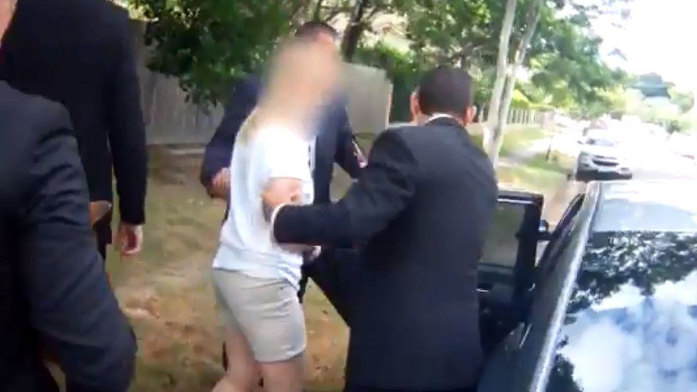 Police officers guide the woman into a car after her arrest