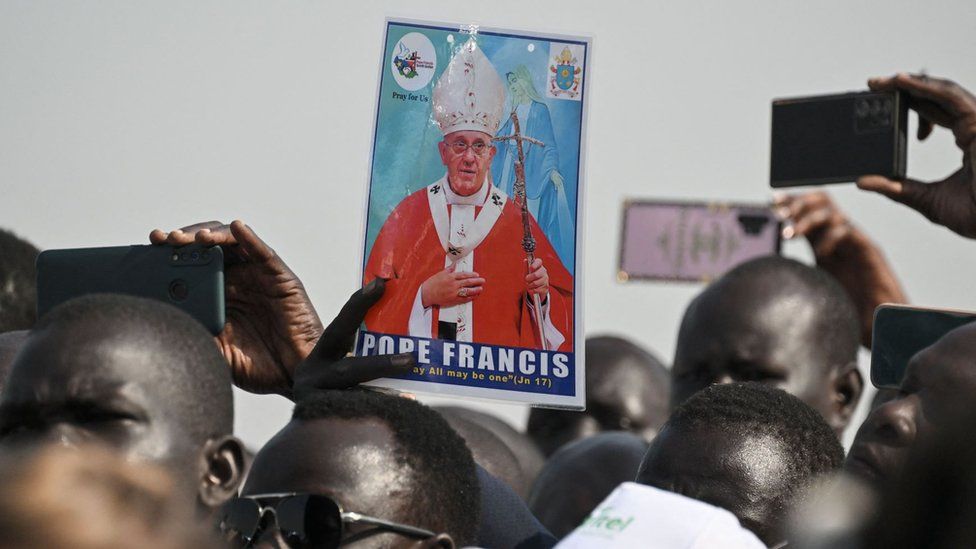 A man holds a picture of Pope Francis as a crowd gathers to welcome him upon his arrival at the Juba International Airport in Juba, South Sudan, on February 3, 2023