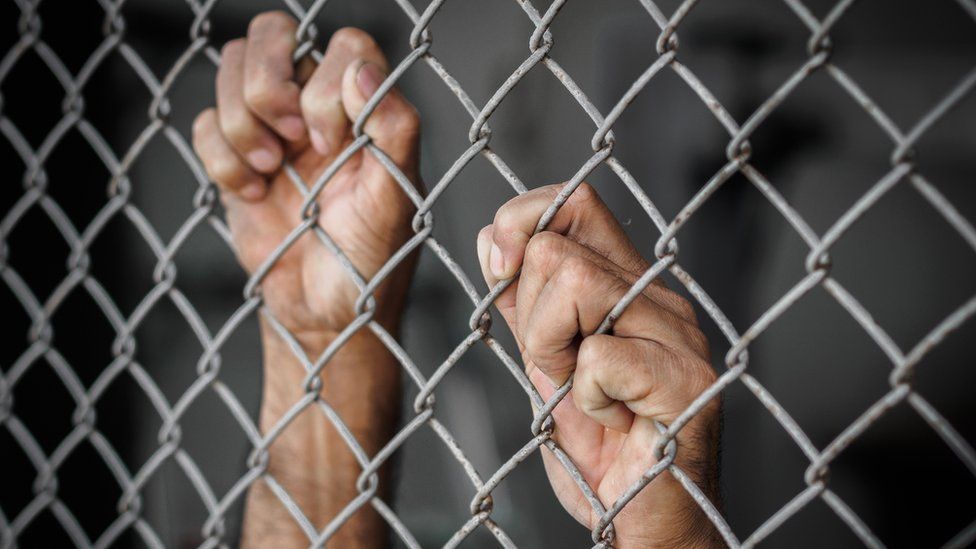 Male hands hold onto a chain link fence