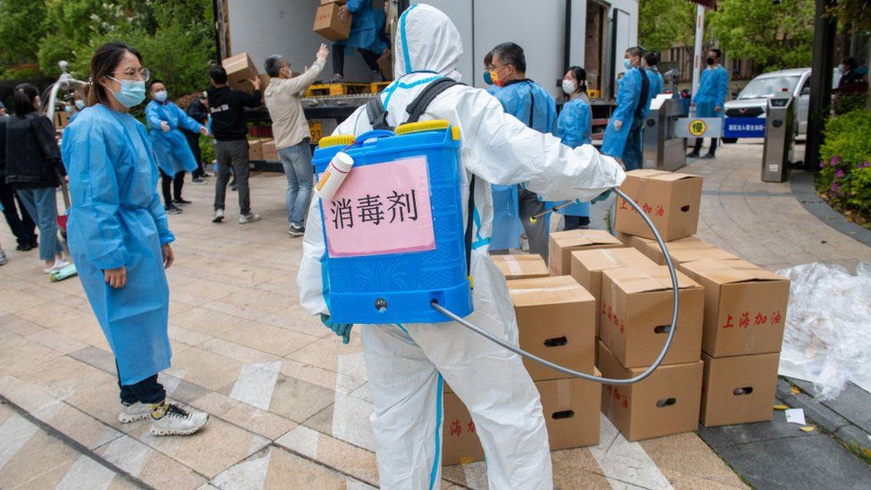 A man in a Hazmat suit sprays disinfectant on a pile of cardboard boxes in China