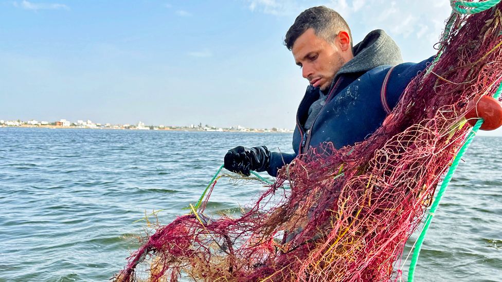 Fisherman Oussama Dabbebi on his boat holding a net in Sfax, Tunisia