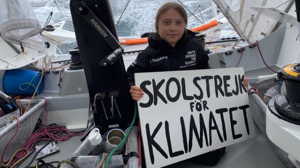 Greta Thunberg holds her "school strike for climate" sign onboard the racing boat Malizia II in the Atlantic Ocean