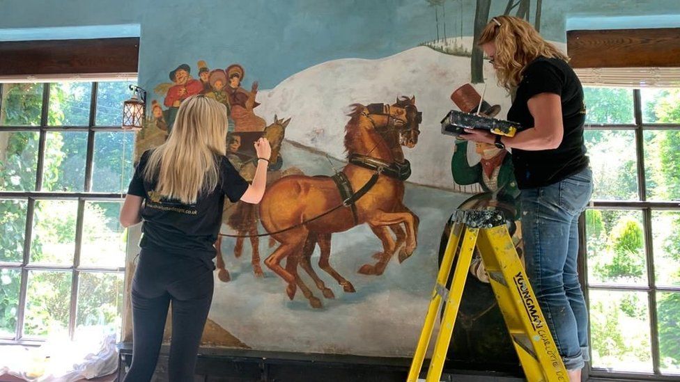Artists Sarah Daniels and Sarah Hodgkins restore part of the mural showing a coach struggling up the road from Scotch Corner in the snow