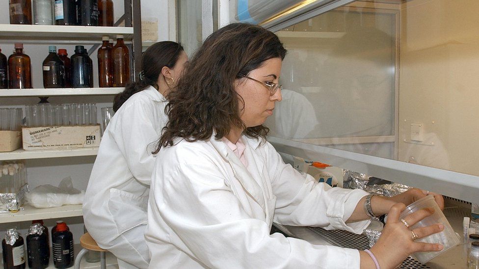 Two women handle chemicals behind a protective screen in a lab in Tunis.