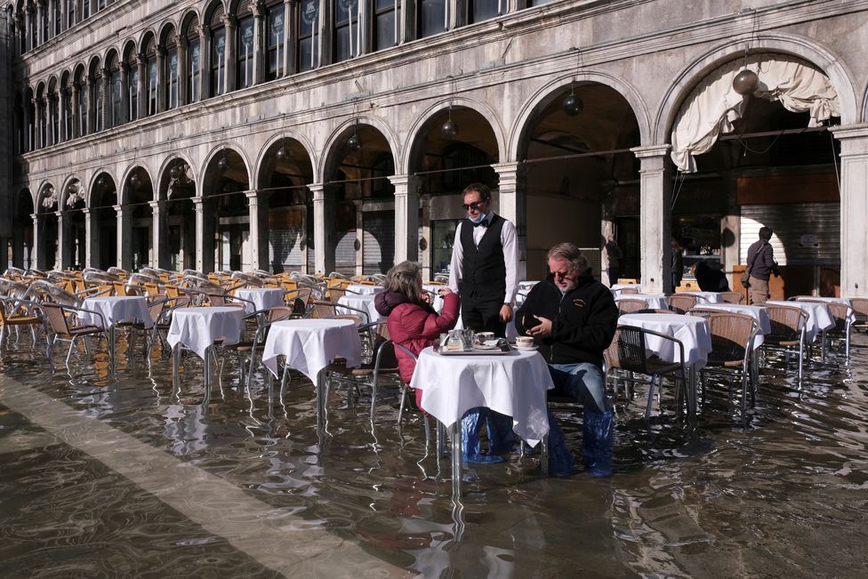 People sit at a cafe in a flooded St Mark's Square during seasonal high tides in Venice, Italy, on 5 November 2021