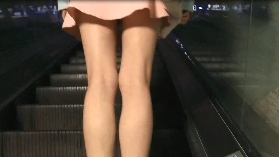 A still from the video, showing a woman's legs, shot from behind her on an escalator