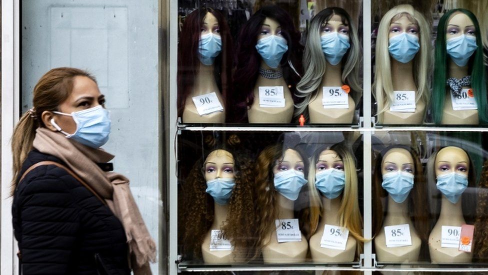 A woman wearing a protective face mask walks past a shop window displaying mannequin heads with masks in Paris, France, 28 October 2020