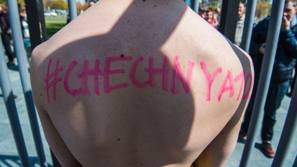 An activist stands naked, wrapped in a rainbow flag, in a mock cage in front of the Chancellery in Berlin on April 30, 2017, during a demonstration calling on Russian President to put an end to the persecution of gay men in Chechnya