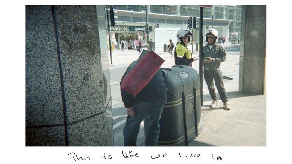 One of Sunny's snapshots showing a homeless man rummaging in a bin, with the handwritten title: "This is life we live in."