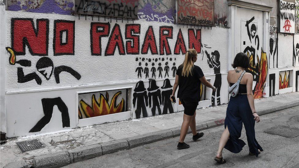 Women walk past the slogan "They shall not pass", which has been spray-painted across various walls in Exarchia.