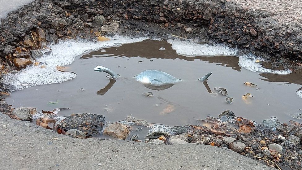 A toy Loch Ness Monster in a pothole