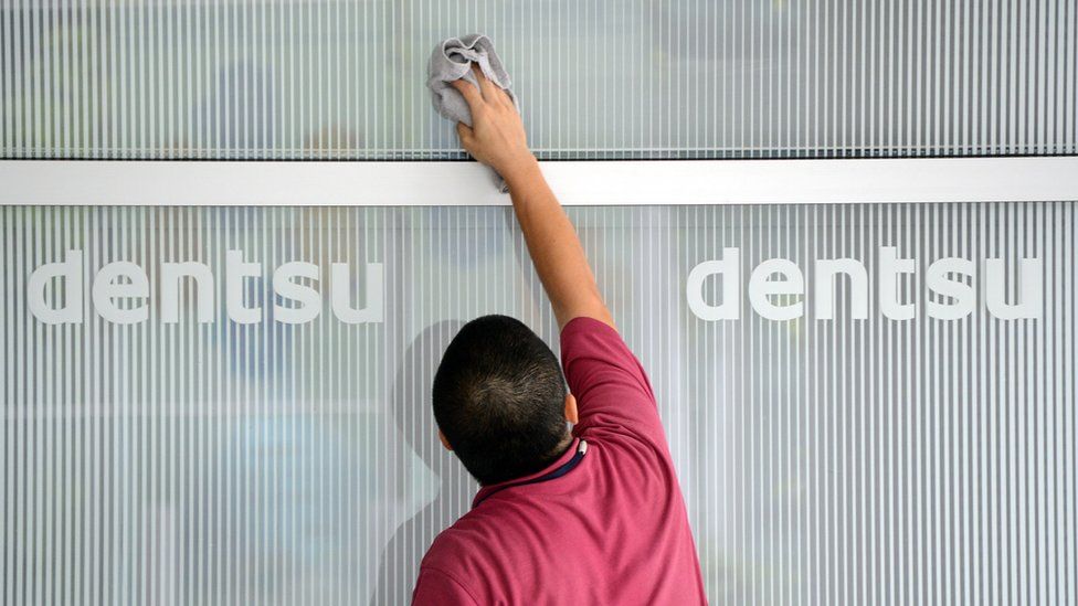 This picture taken on July 14, 2012, shows a man cleaning a window at an entrance of the headquarters of Japan's top advertising agency Dentsu