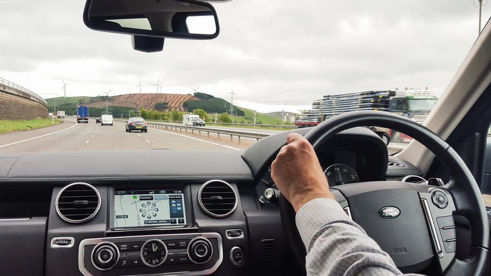 A view from a Land Rover Discovery of a man driving on the M74 motorway, approaching the Clyde Wind Farm, with light traffic on the road.