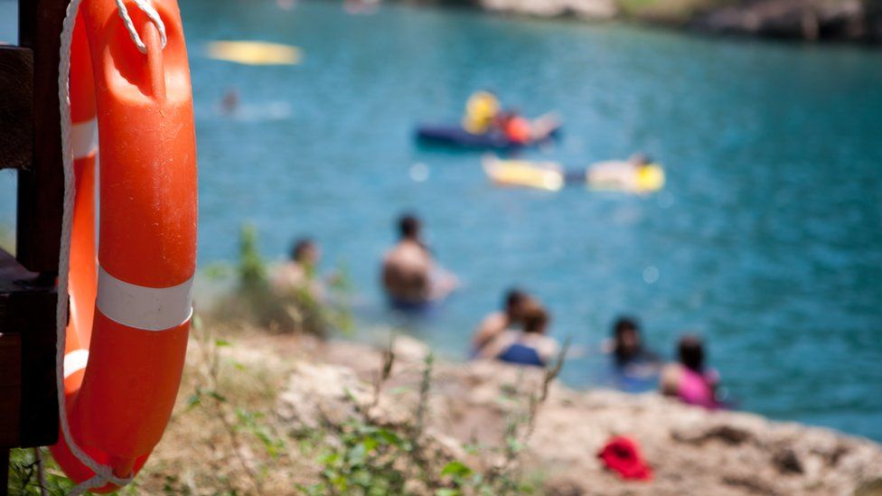 A bright orange life buoy hung on a dock overlooking a group of swimming people