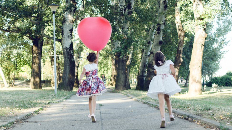 Two young girls walking through a park holding a balloon