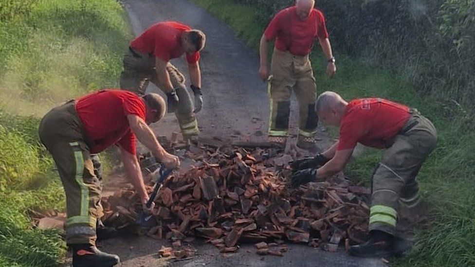 Four firefighters working to clear a large amount of flytipping from a narrow, single track country lane.